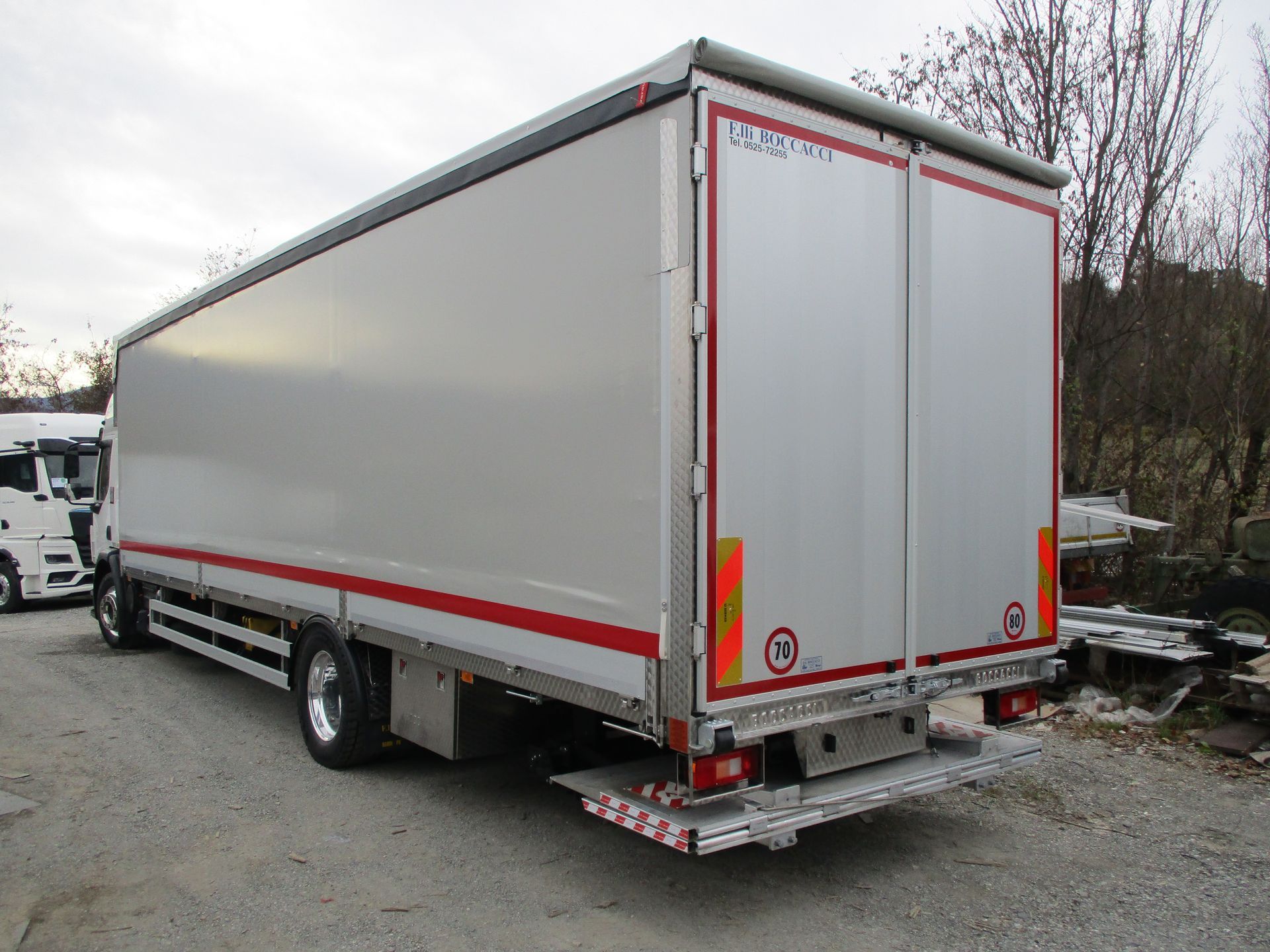 Un furgone bianco parcheggiato su un piazzale ghiaioso, visto da dietro, con finiture rosse e segnaletica di emergenza sulle portiere.