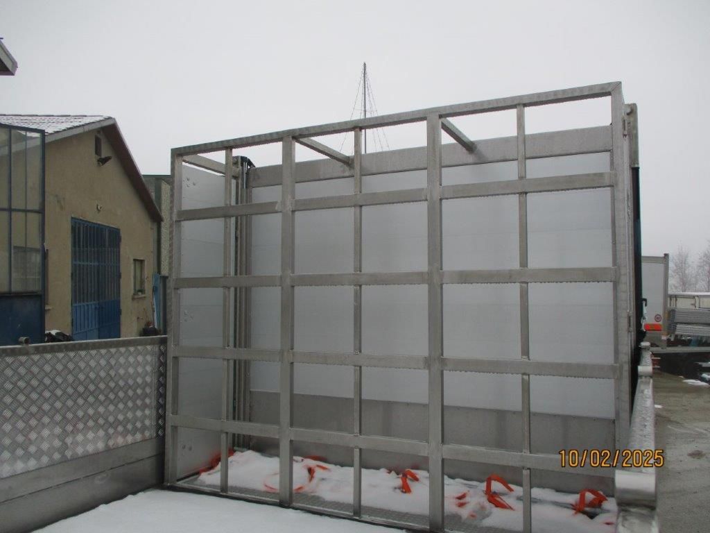 Una grande struttura metallica rettangolare si erge all'aperto su una superficie innevata vicino a un edificio.