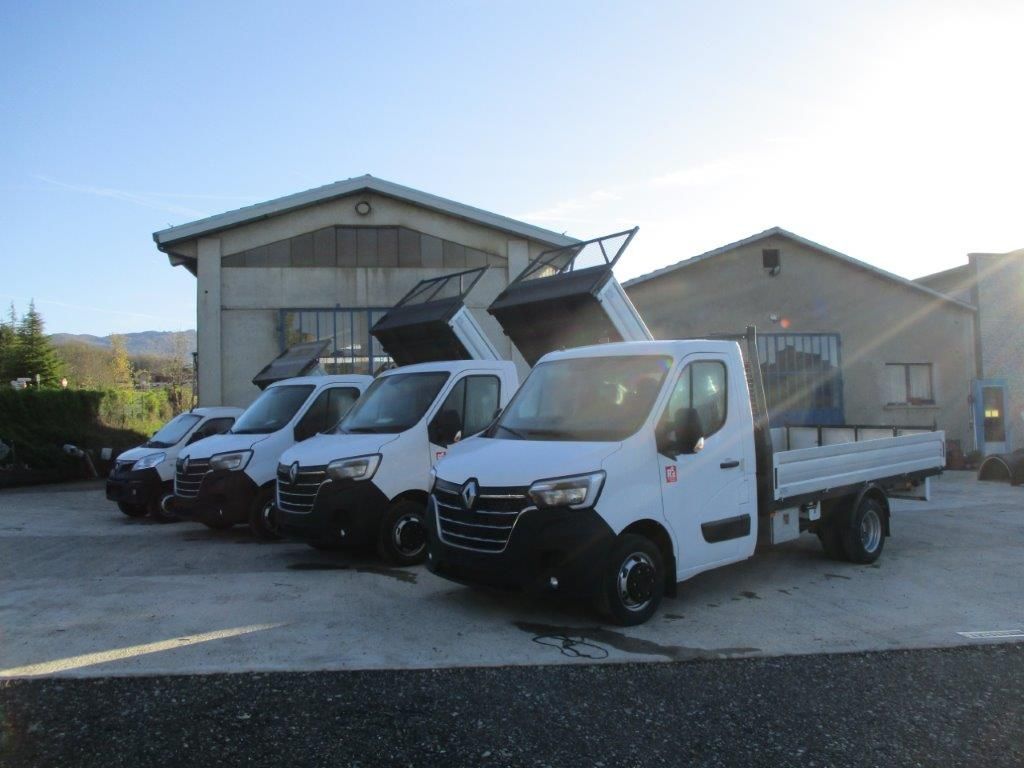 Una fila di autocarri ribaltabili Renault bianchi parcheggiati in fila su un piazzale ghiaioso di fronte a degli edifici industriali.