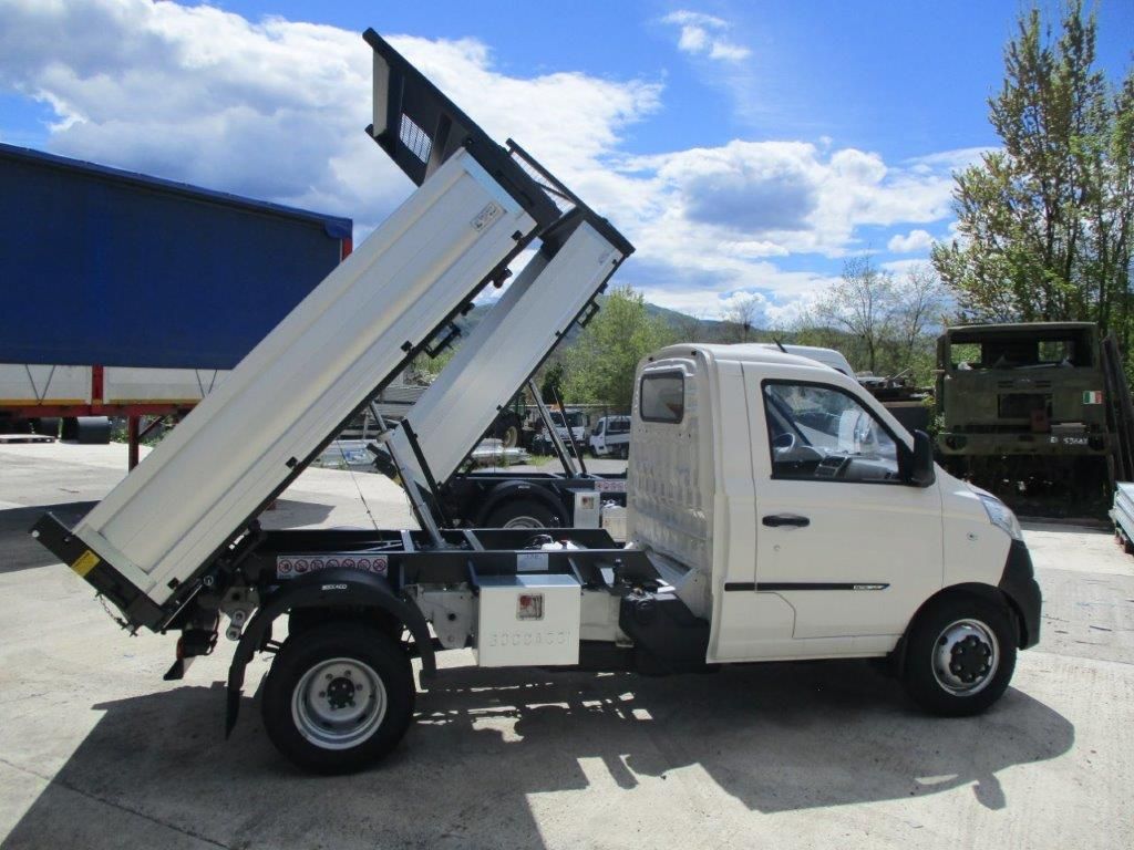 Un piccolo camioncino bianco con il cassone sollevato, parcheggiato all'aperto in una giornata di sole.