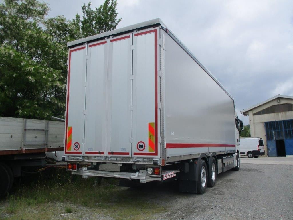 Un furgone bianco per le consegne è parcheggiato su un piazzale ghiaioso accanto a un rimorchio, visto da dietro.