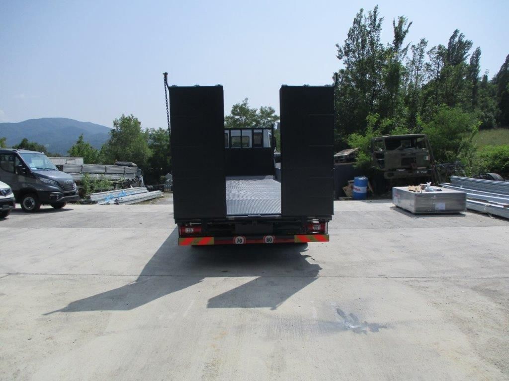 Vista posteriore di un rimorchio a pianale nero con rampe metalliche verticali, parcheggiato in un soleggiato piazzale industriale adibito a magazzino all'aperto.