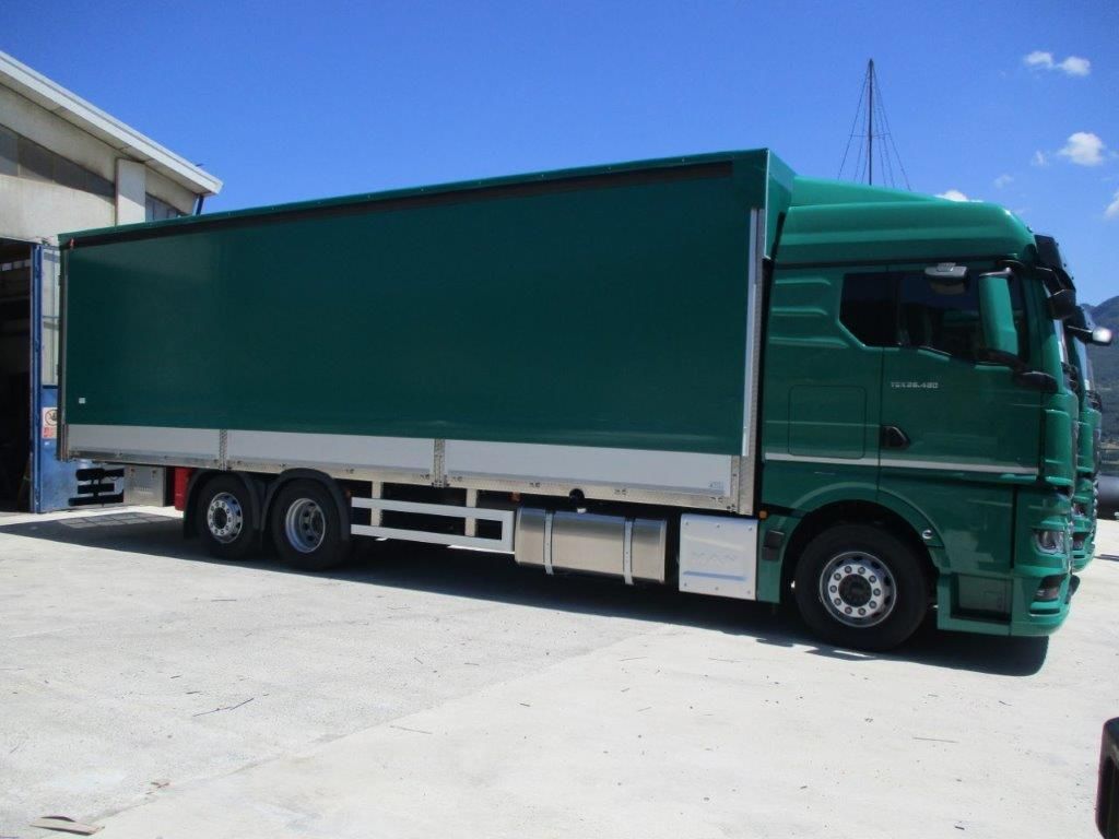 Vista laterale di un camion verde per carichi pesanti parcheggiato su un piazzale di cemento sotto un cielo azzurro e limpido.