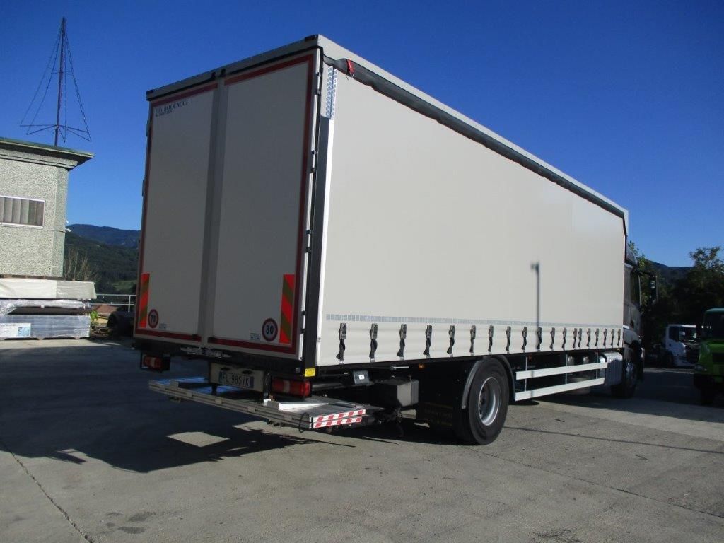 Un furgone bianco parcheggiato, con una copertura laterale in tela, visto dall'angolo posteriore in una giornata di sole.