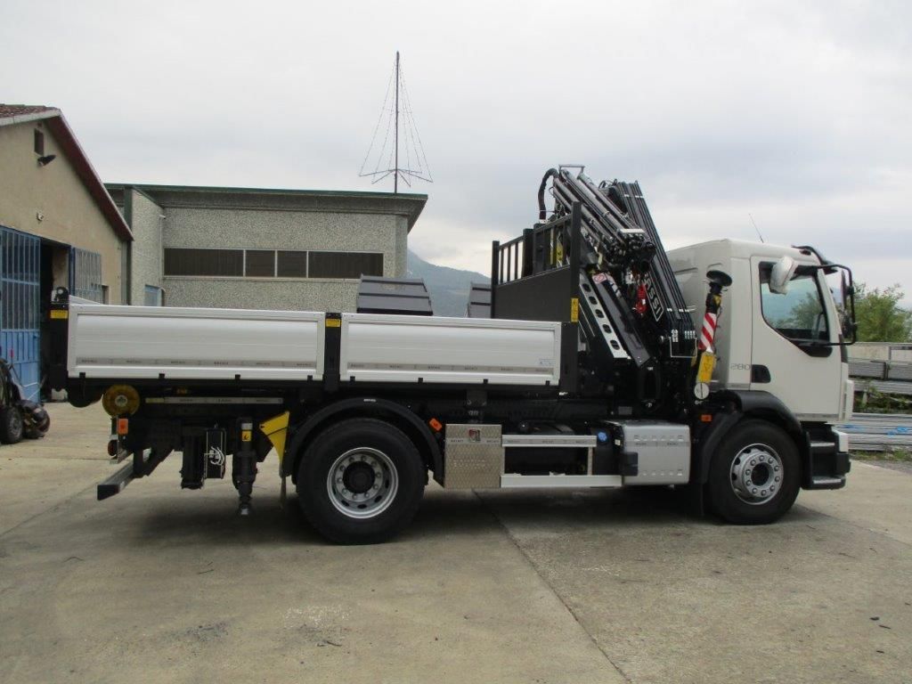 Un autocarro ribaltabile bianco con pianale, dotato di una gru pieghevole nera montata dietro la cabina, parcheggiato su un piazzale asfaltato.