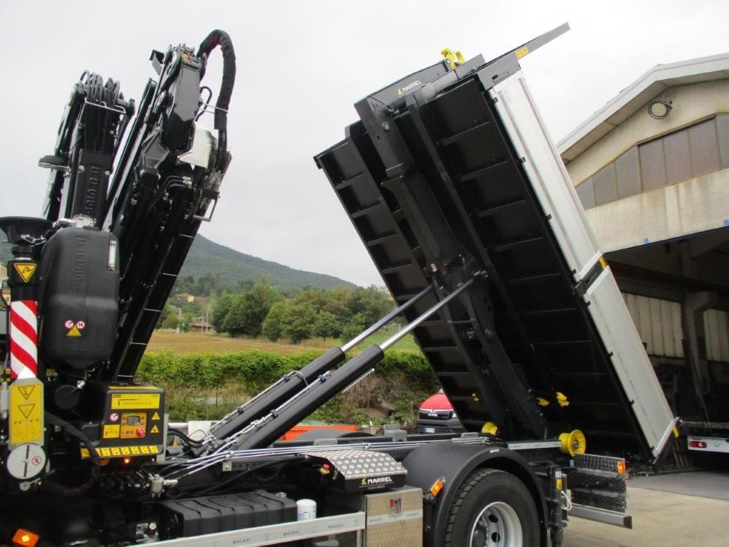 Un camion per carichi pesanti con gru idraulica e il cassone sollevato in posizione di scarico inclinato all'aperto.