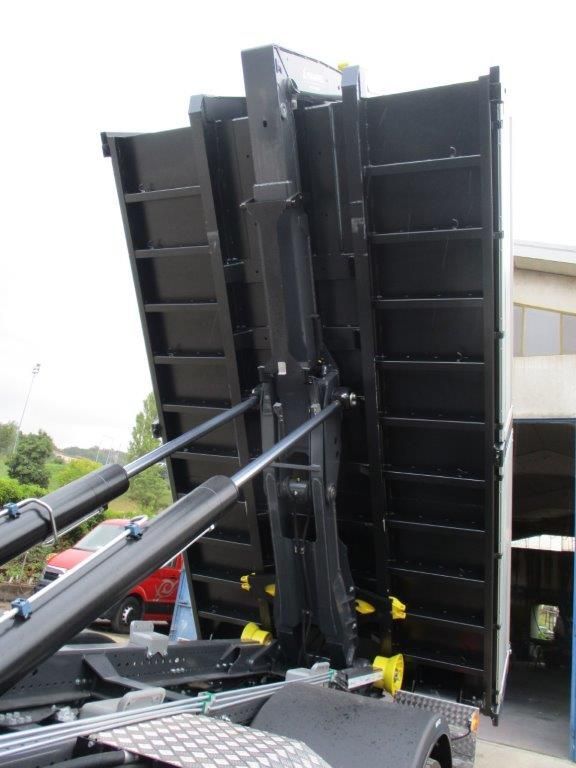 Il cassone di un camion ribaltabile nero è sollevato, mostrando la parte inferiore rinforzata e il meccanismo di sollevamento idraulico.