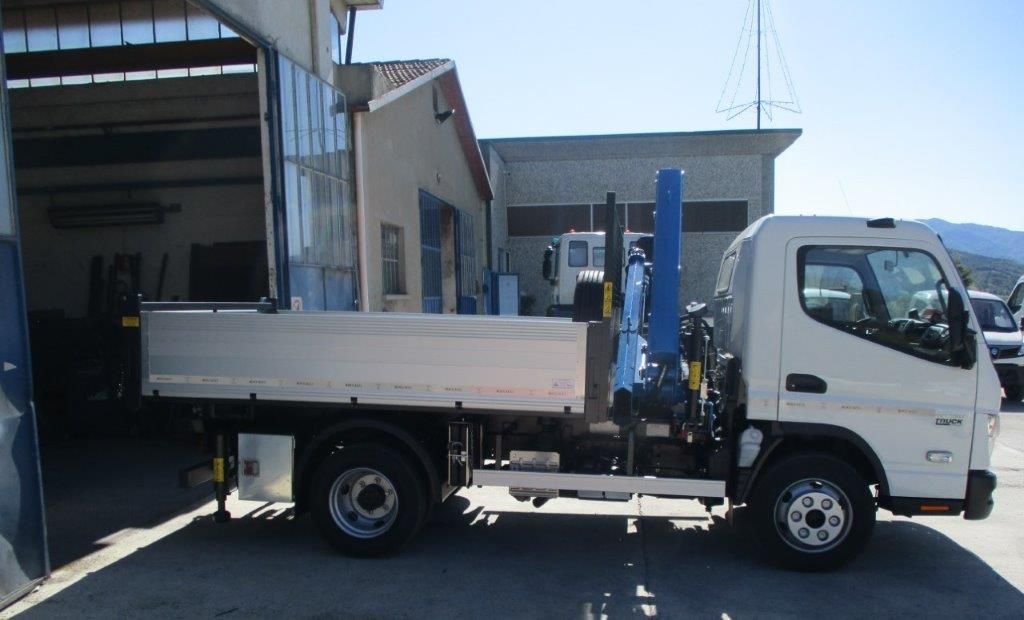 Un camioncino bianco leggero con sponde ribaltabili e gru idraulica montata, parcheggiato davanti a un'officina.
