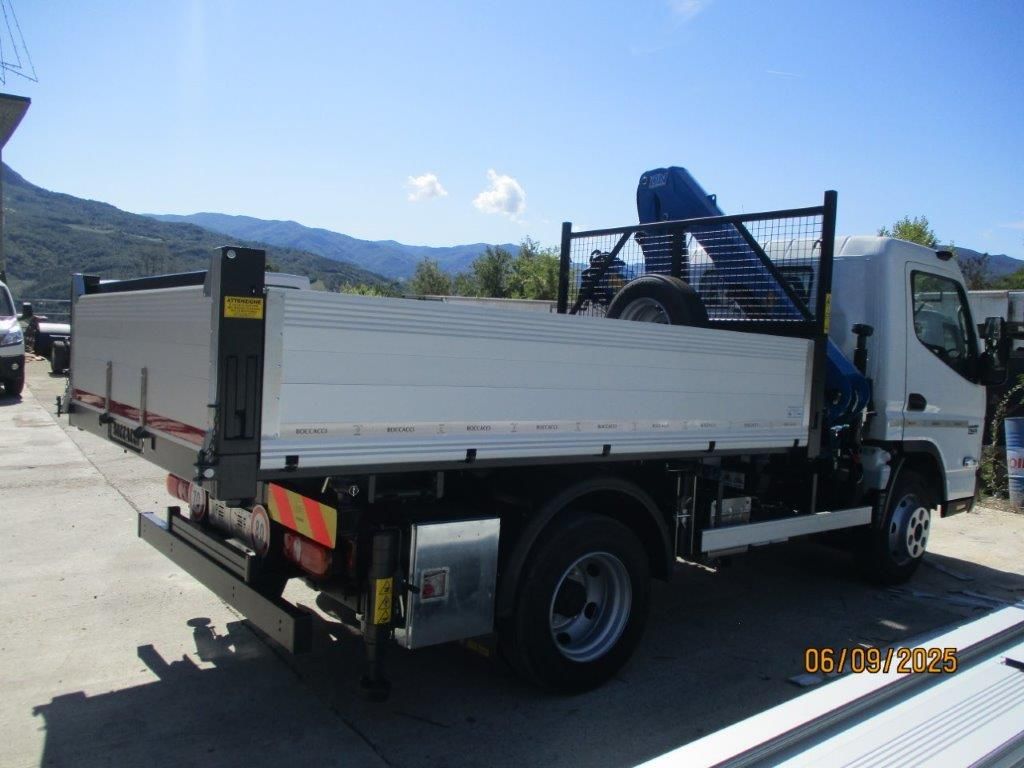 Un autocarro ribaltabile bianco con gru montata, parcheggiato all'aperto su un piazzale di cemento con uno sfondo montuoso.