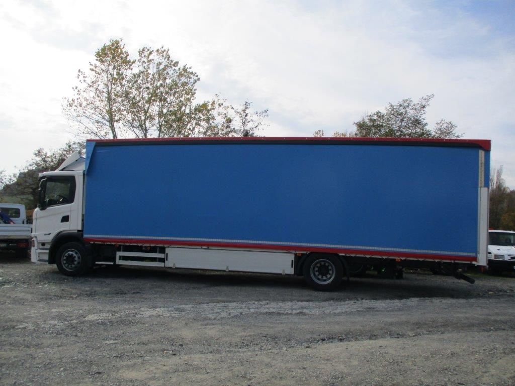 Un camion Scania bianco con un grande cassone di carico blu scuro parcheggiato su un piazzale ghiaioso sotto un cielo nuvoloso.