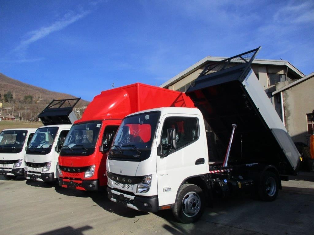 In una giornata di sole, una fila di autocarri ribaltabili Mitsubishi Fuso bianchi e rossi era parcheggiata all'aperto, con il cassone di uno di essi inclinato verso l'alto.