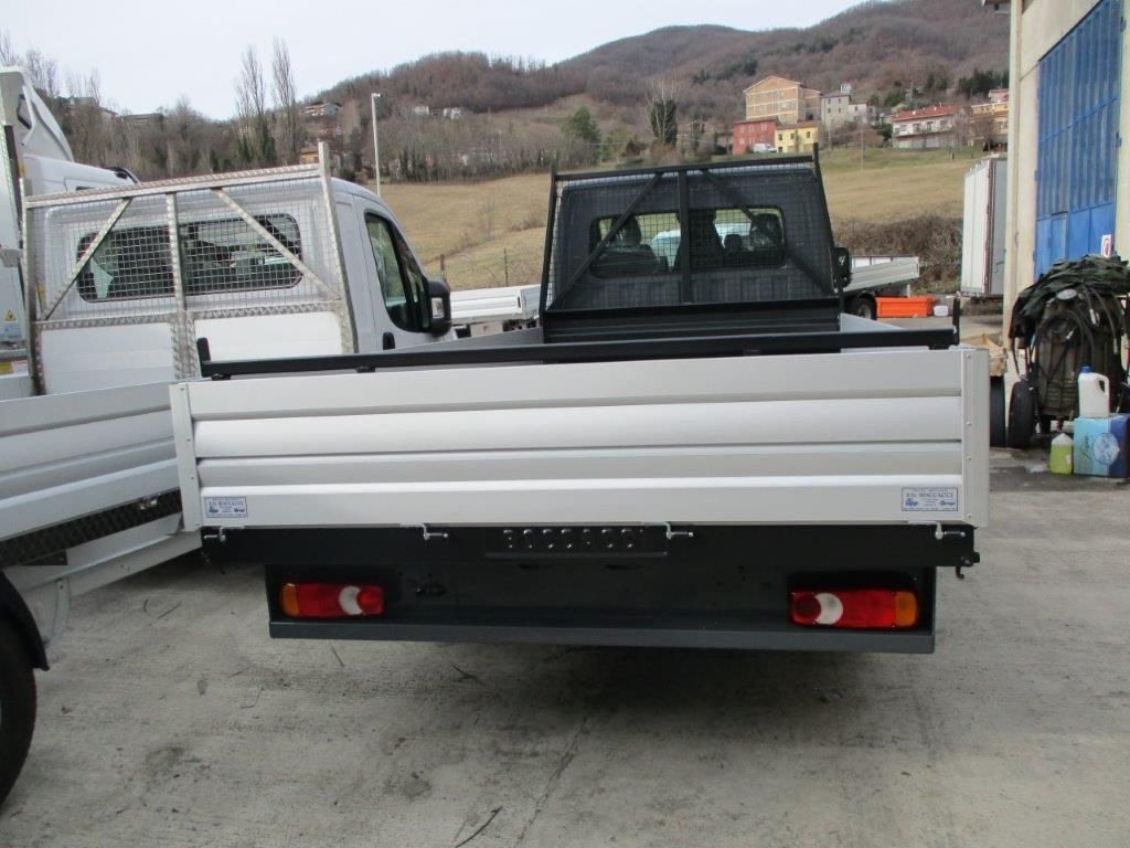 Vista posteriore di un camioncino bianco con pianale, parcheggiato su un piazzale ghiaioso con colline sullo sfondo.