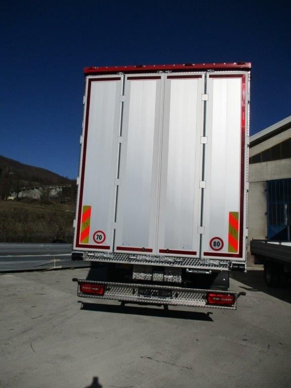 Il portellone di un semirimorchio bianco a pannelli verticali, parcheggiato all'aperto in una giornata di sole, con cerchi rossi che indicano il limite di velocità 