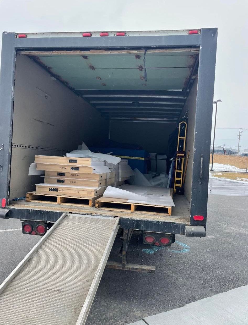 Arrière d'un camion de livraison avec rampe déployée, chargé de palettes et de matériaux.