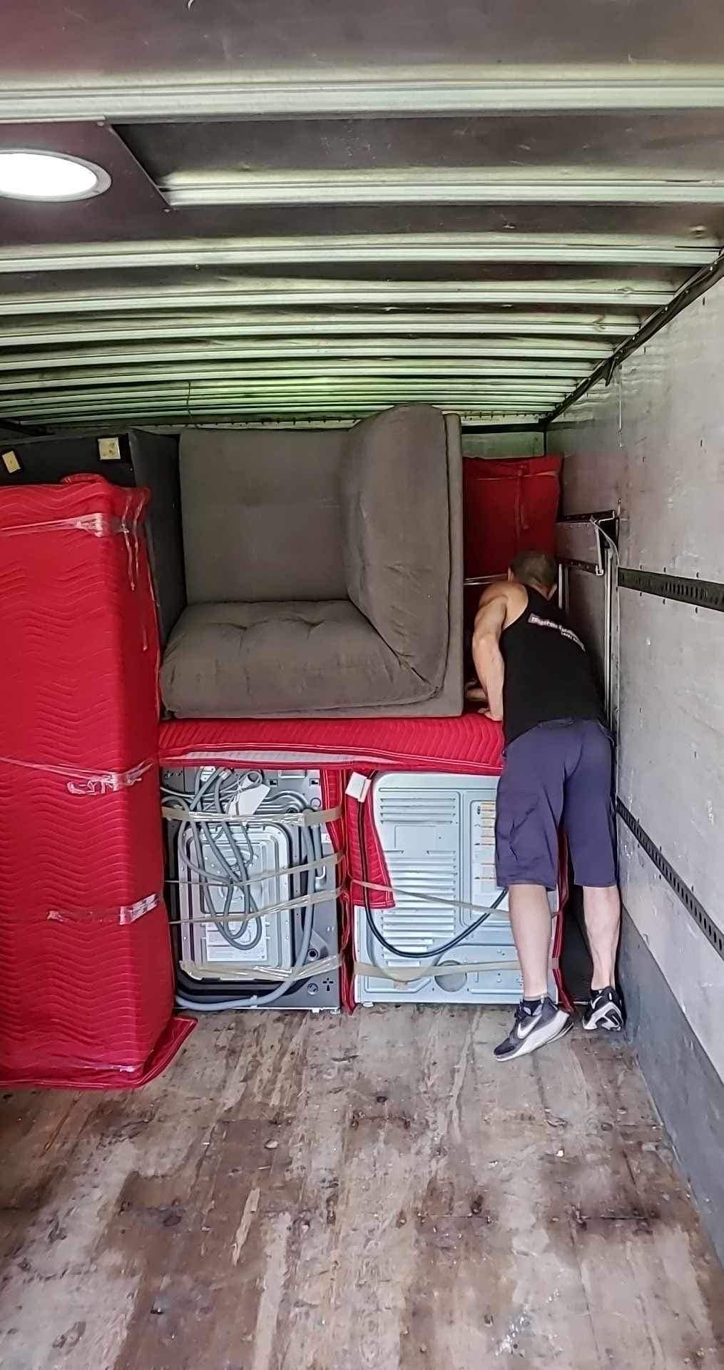 Personne chargeant des meubles dans un camion : canapé, appareils électroménagers emballés et boîtes.