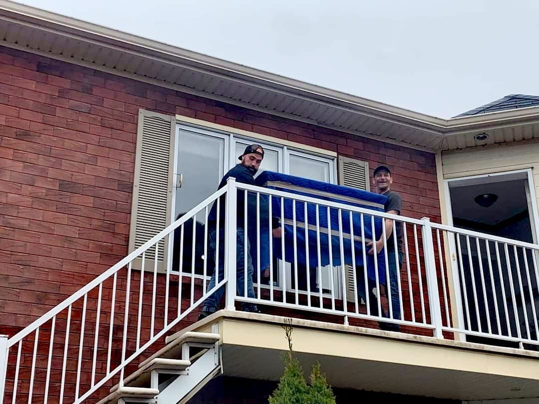 Deux hommes transportant un objet bleu sur le balcon d'une maison en briques.