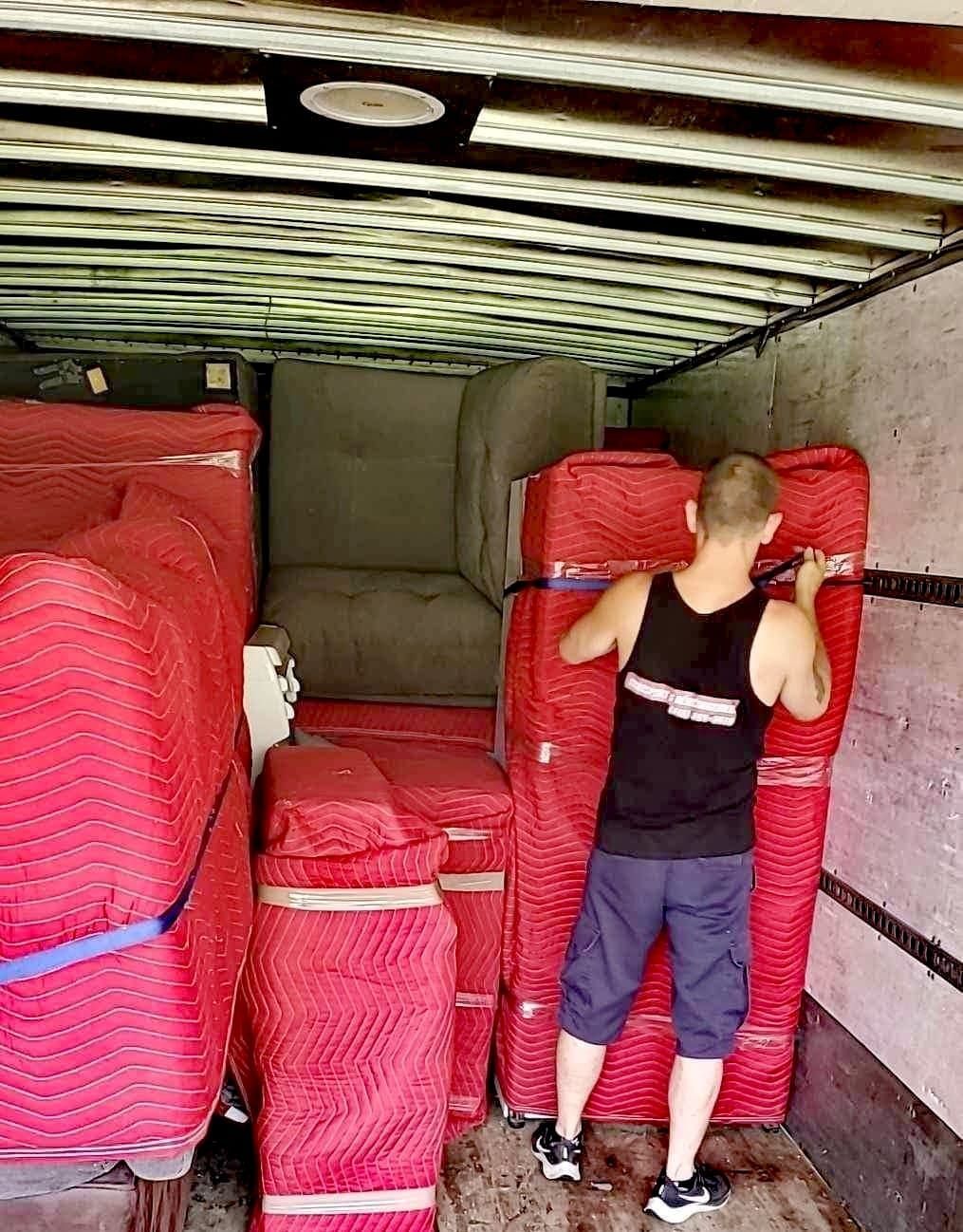 Un homme charge un camion de déménagement, des meubles enveloppés dans des coussinets rouges.