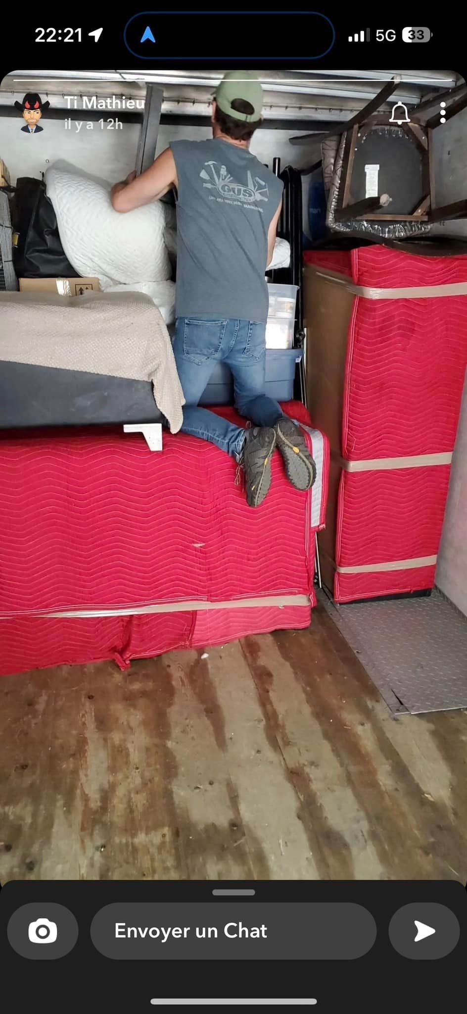 Un homme portant un chapeau vert est à l'intérieur d'une remorque en train de charger des meubles. On aperçoit les coussins rouges et les tapis marron.