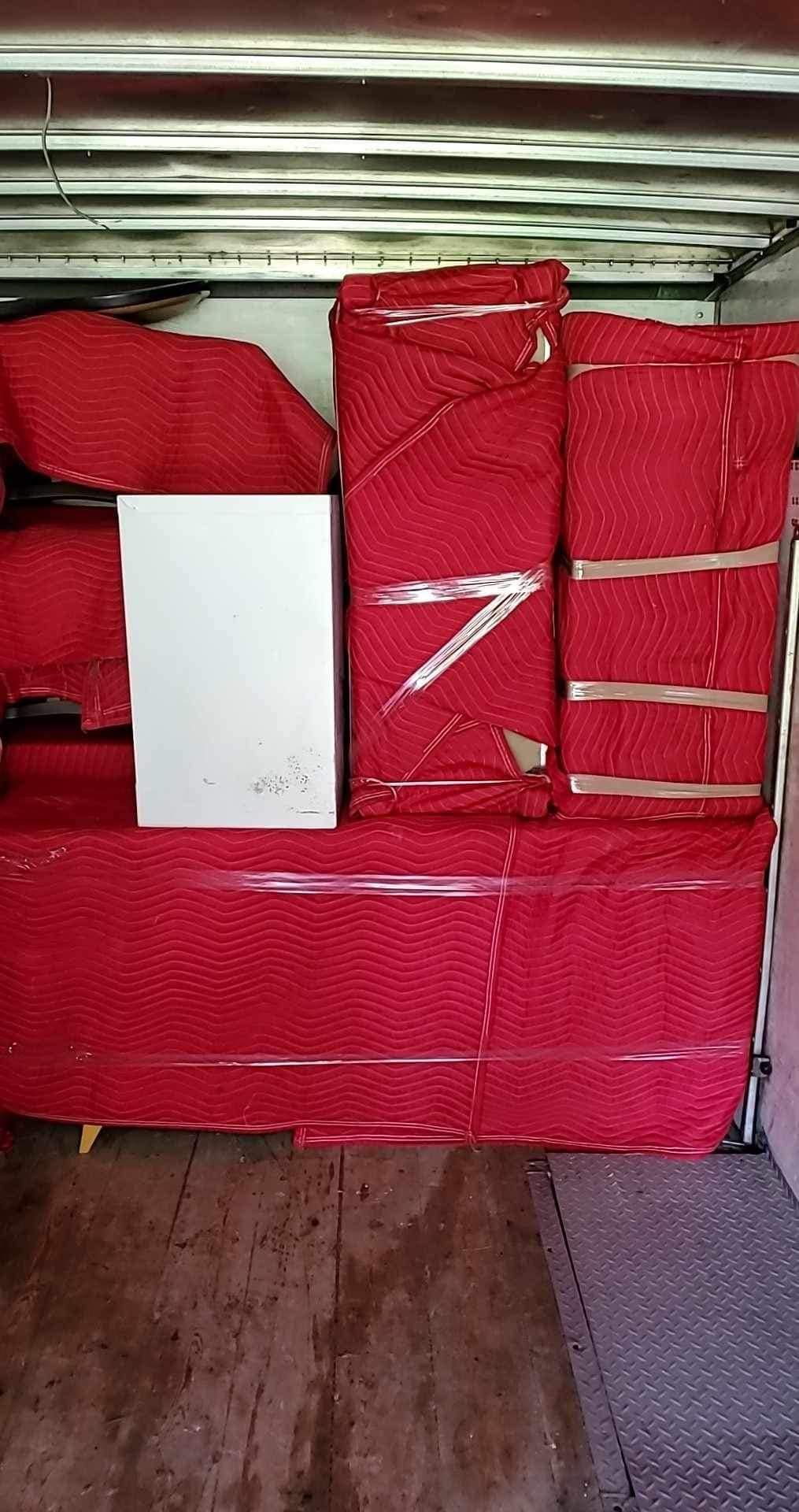 À l'intérieur d'un camion de déménagement, les meubles sont enveloppés dans des couvertures rouges et fixés avec du ruban adhésif. On aperçoit une armoire blanche.