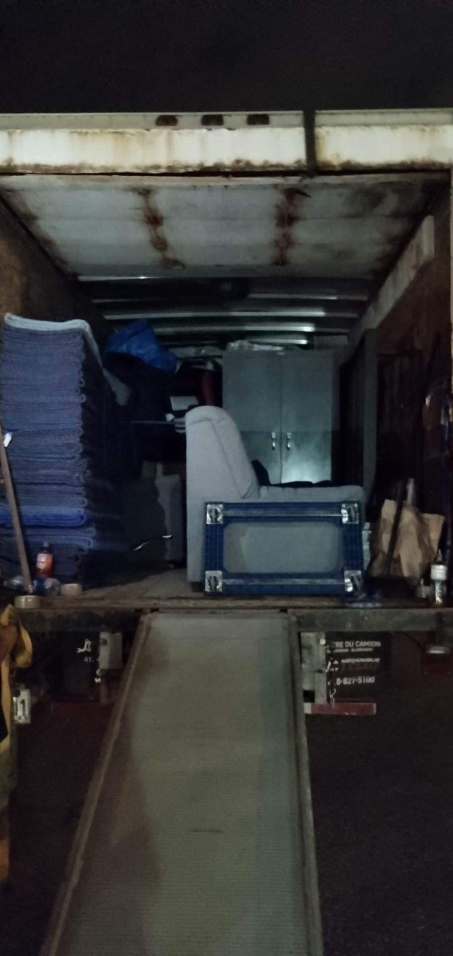 À l'intérieur d'un camion de déménagement, il y a des meubles, des couvertures bleues et une rampe.