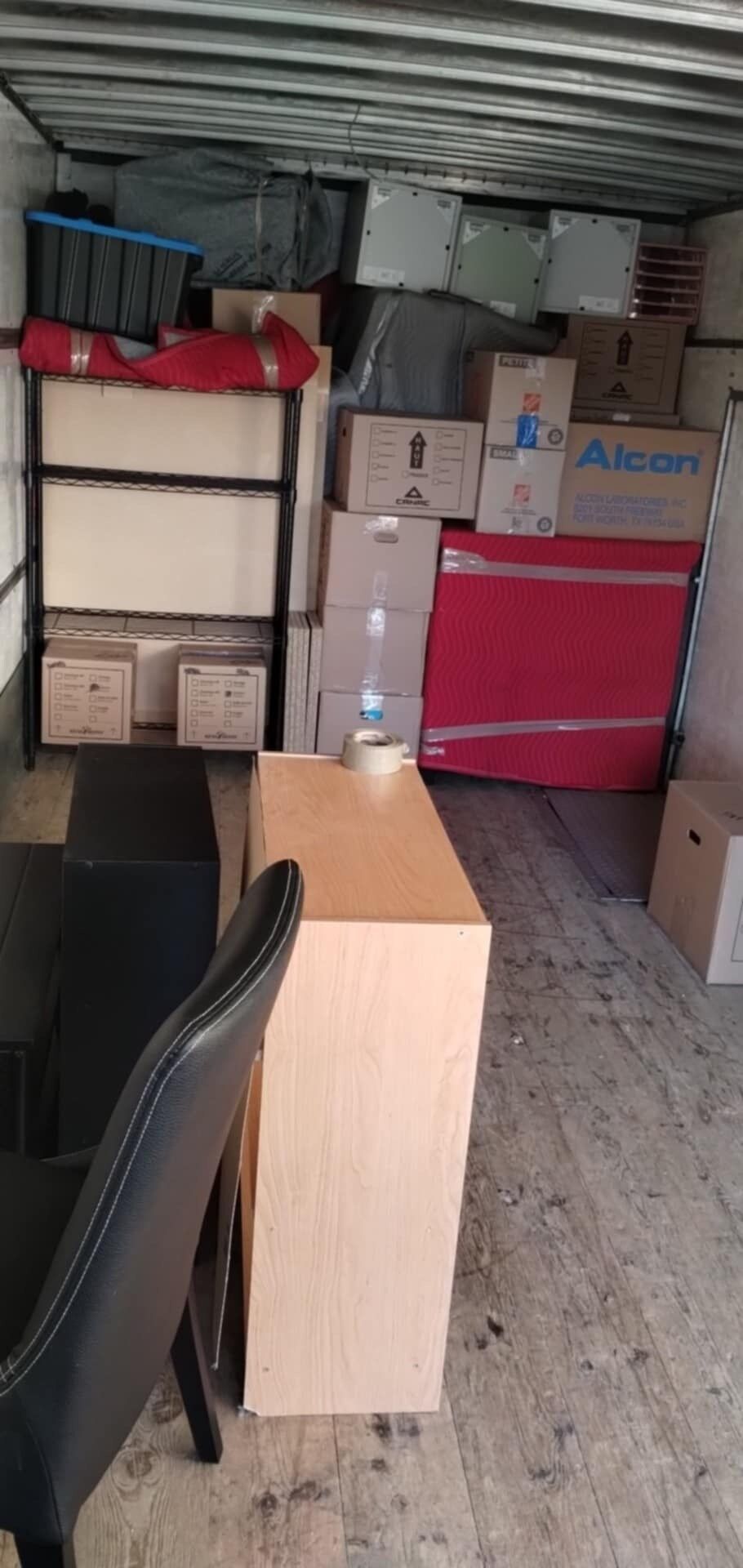 Intérieur d'un camion de déménagement rempli de meubles, de cartons et d'une étagère. Une chaise est au premier plan.
