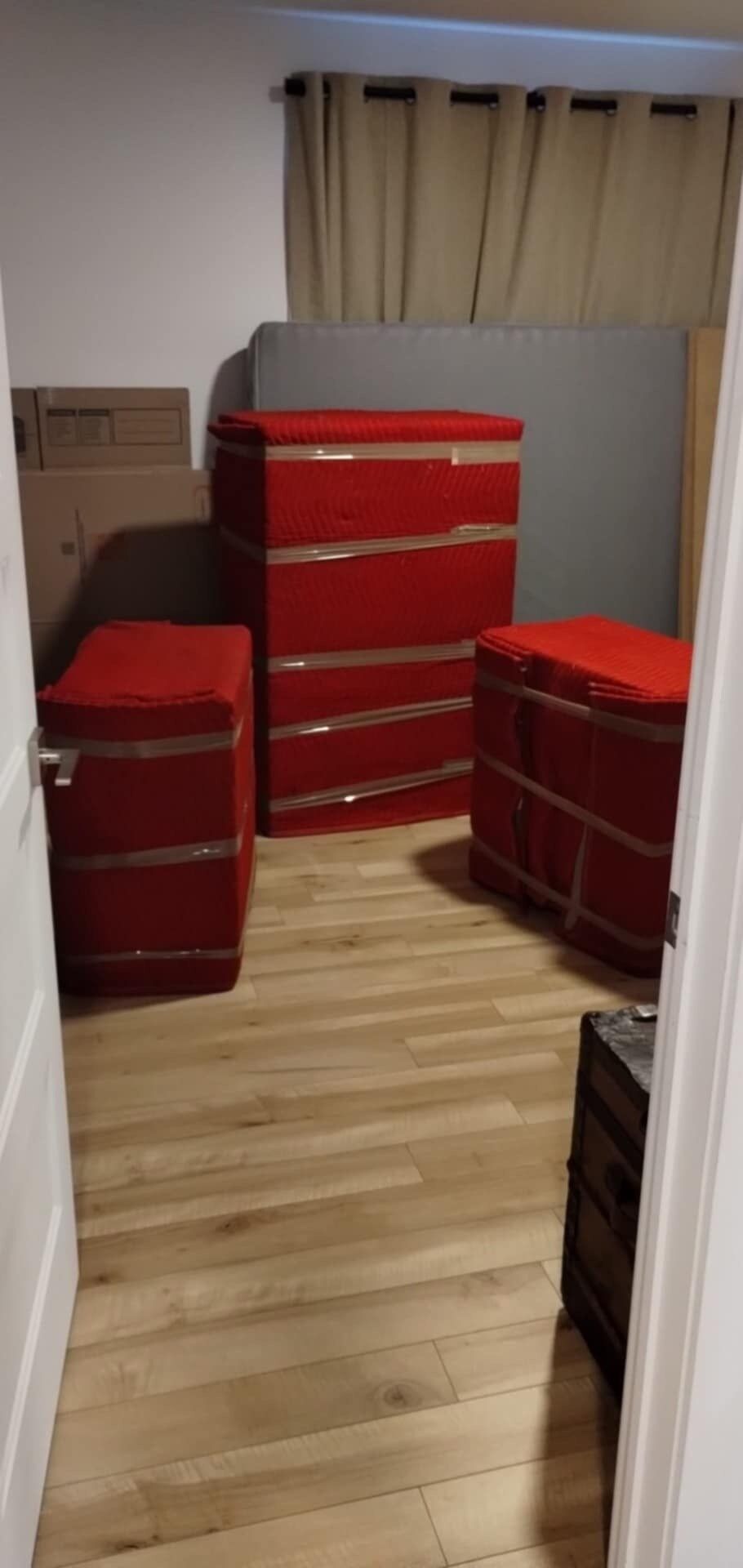 Pièce avec trois coffres rouges emballés dans du plastique, une boîte en carton et un plancher en bois.