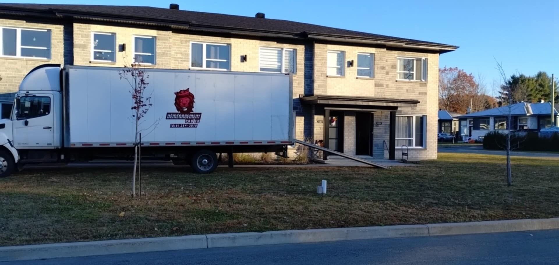 Camion de déménagement stationné devant un immeuble en briques, rampe déployée.