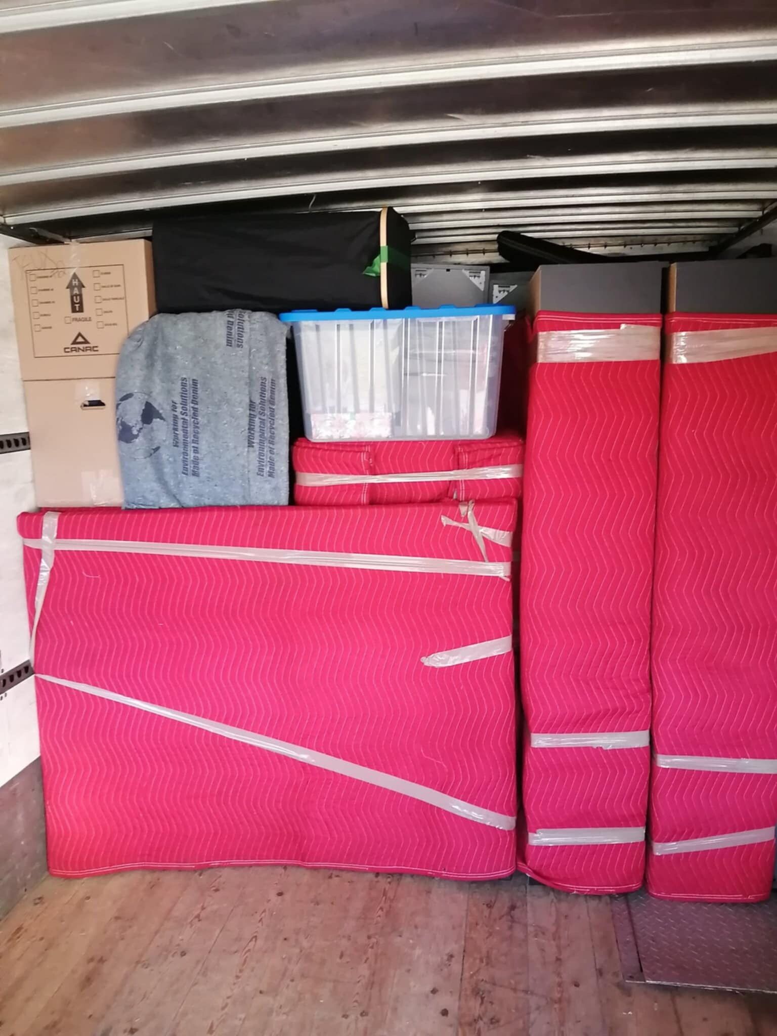 L'intérieur d'un camion de déménagement rempli de cartons emballés, de conteneurs et de meubles emballés en rouge et blanc.