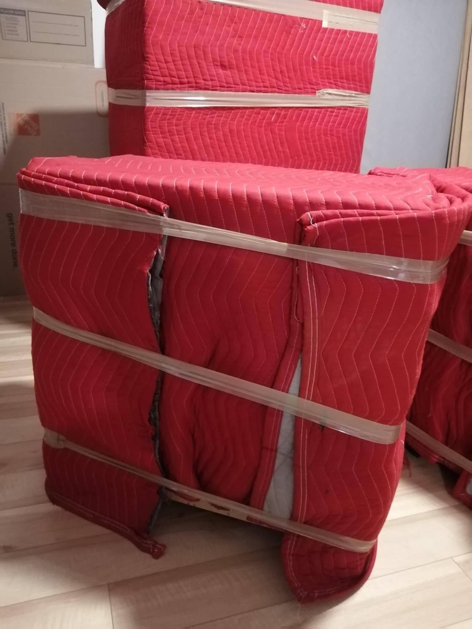 Meubles rouges enveloppés dans des couvertures de déménagement, fixés avec du ruban adhésif, à l'intérieur d'une maison.