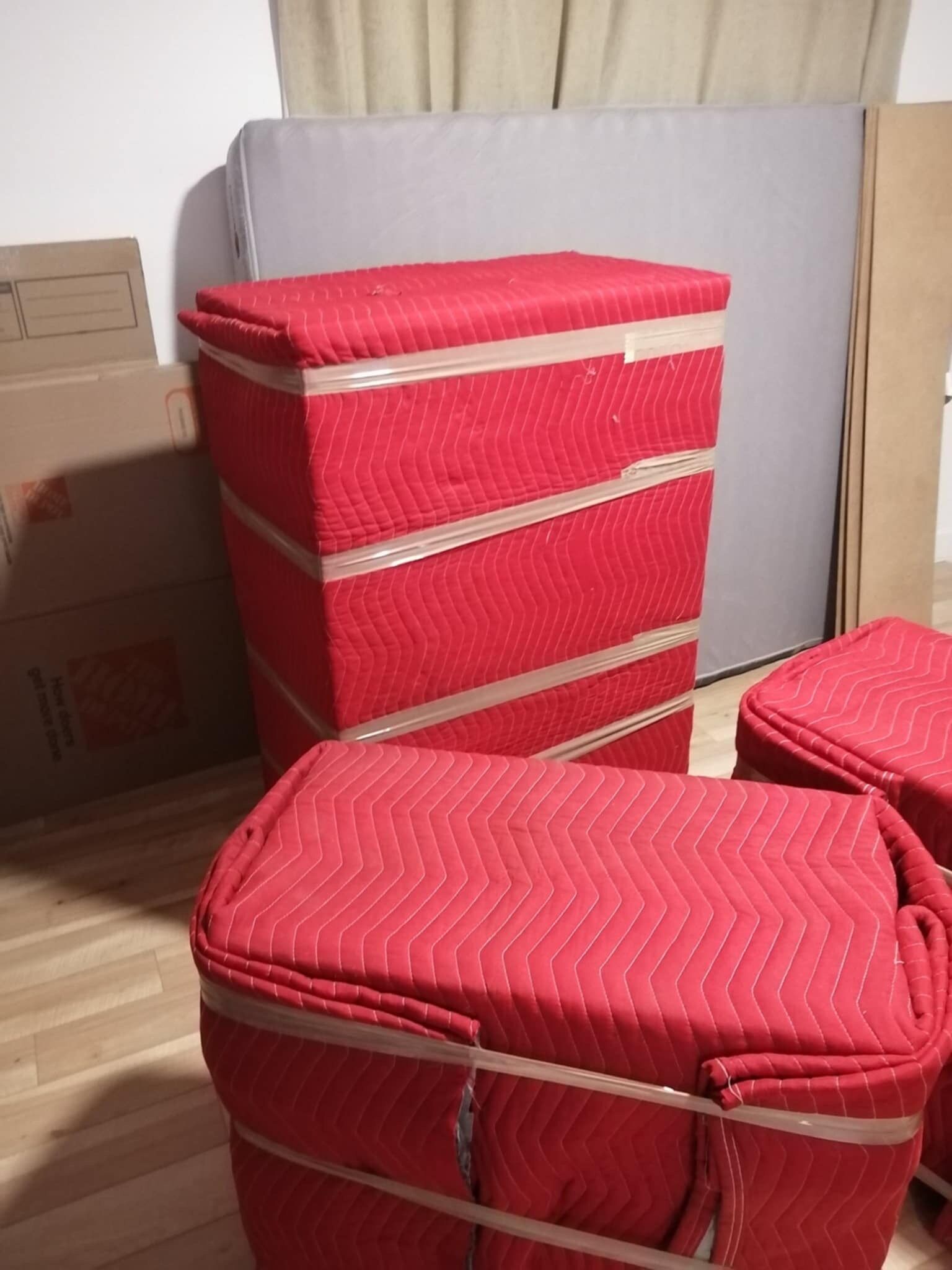 Meubles recouverts de rouge et enveloppés de ruban adhésif, prêts à être déplacés. Boîtes et autres objets dans une pièce.