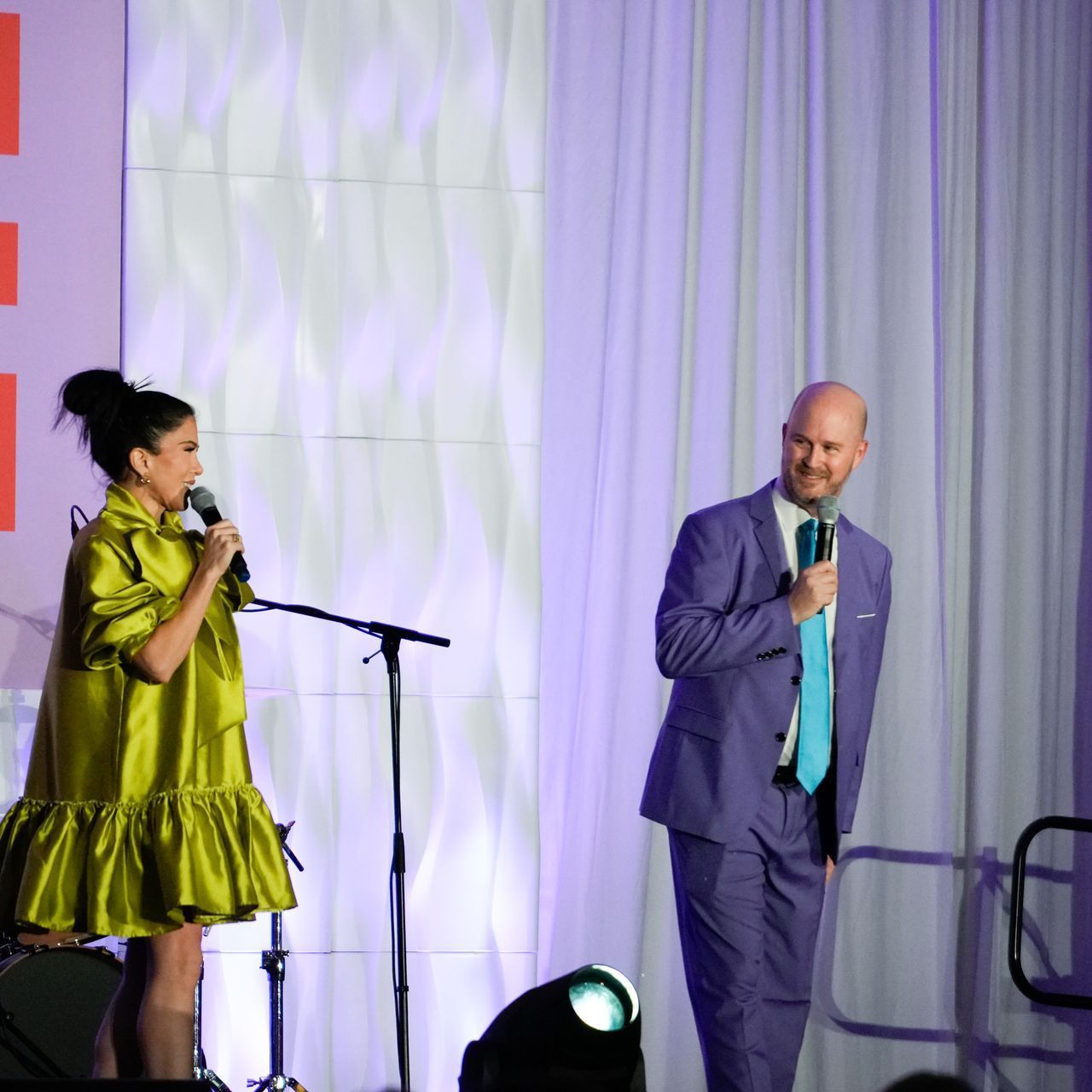 A man in a suit stands next to a woman singing into a microphone