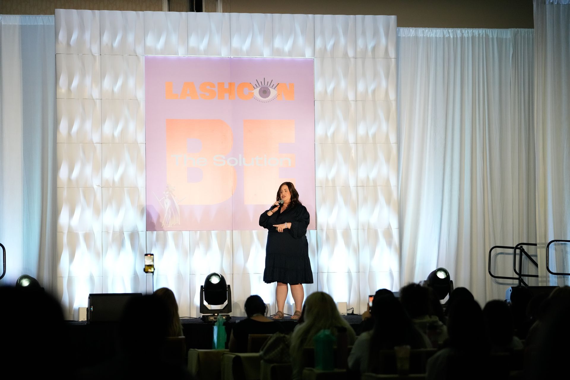 A woman is standing on a stage talking into a microphone.