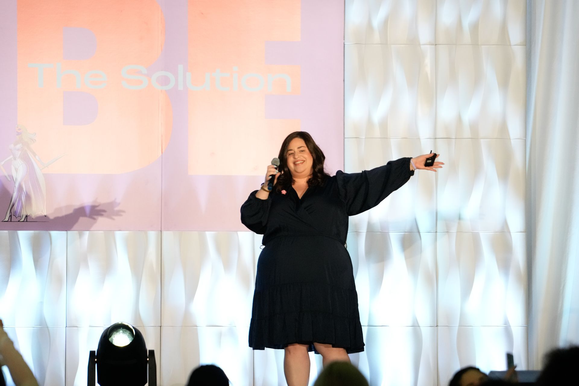 A woman in a black dress is standing on a stage holding a microphone.