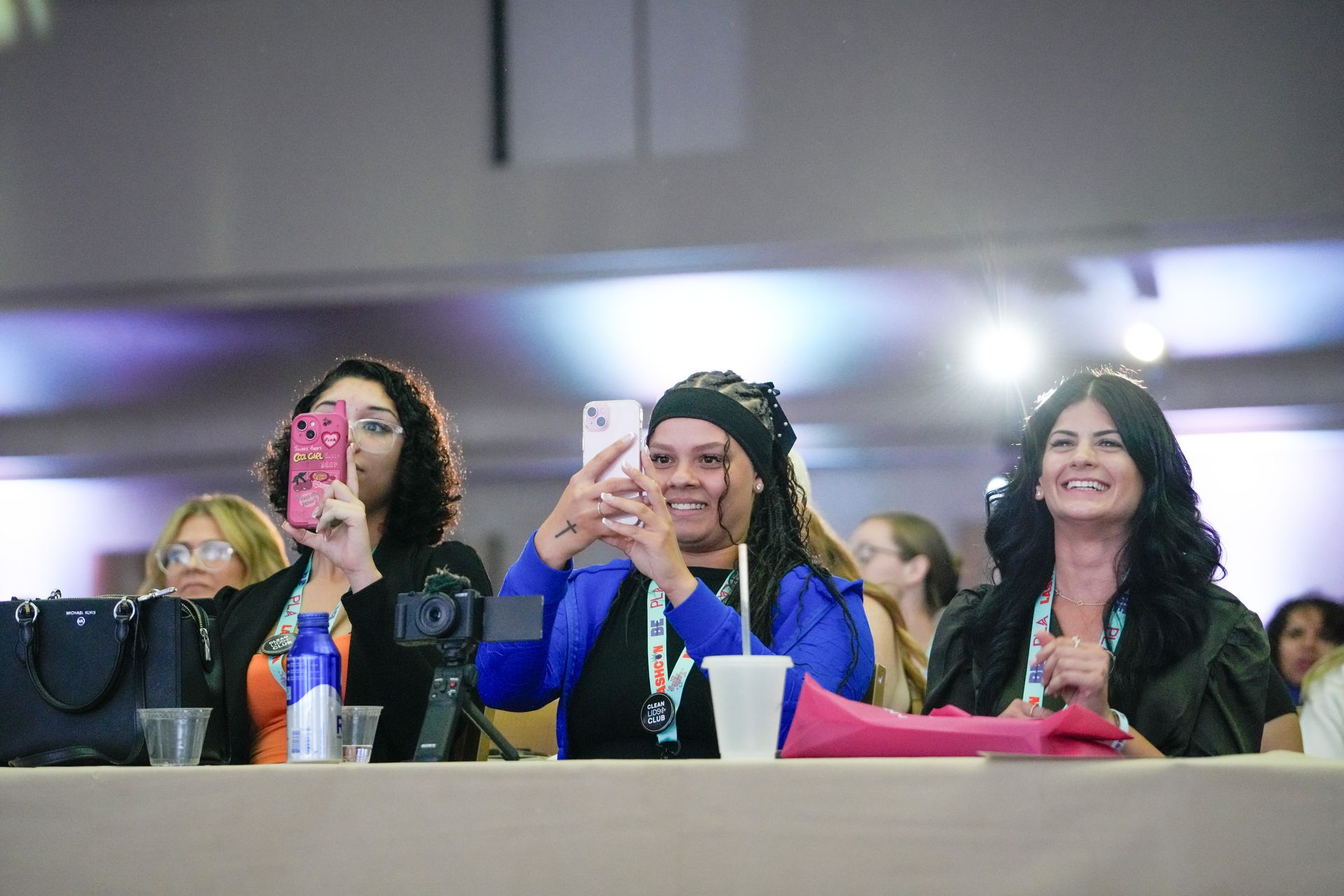A group of women are sitting at a table taking pictures with their cell phones.