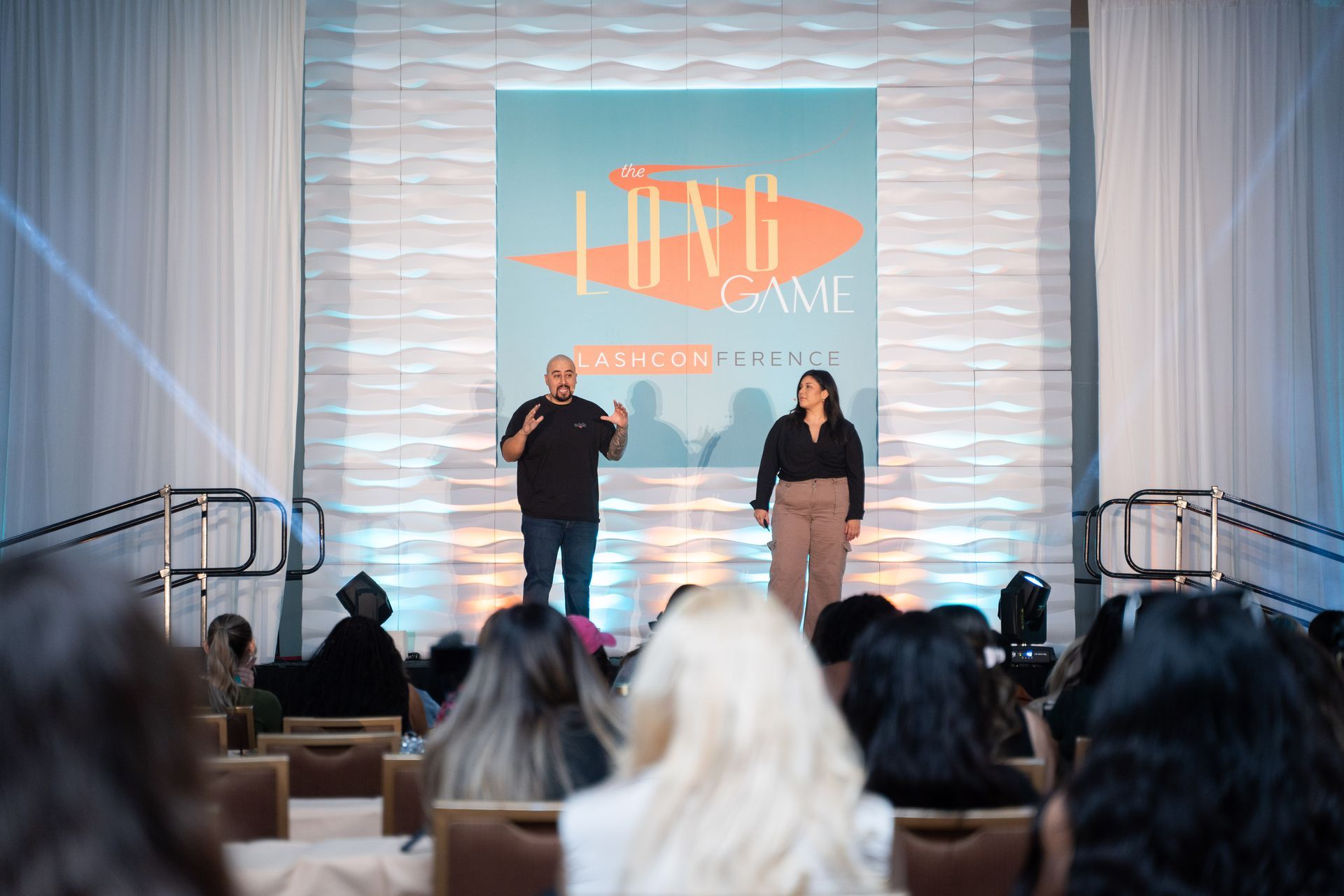 A man and a woman are standing on a stage in front of a crowd.