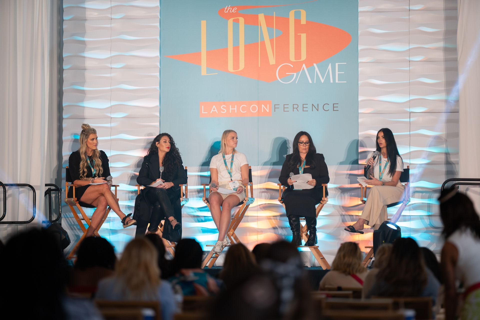 A group of women are sitting on a stage at a long game fashion conference.