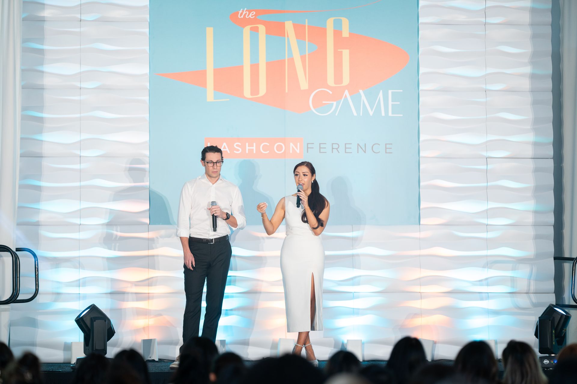 A man and a woman are standing on a stage talking into microphones.