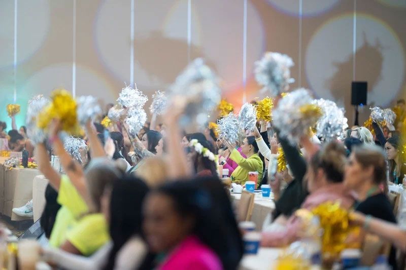 People cheering with silver and gold pom-poms at a conference.