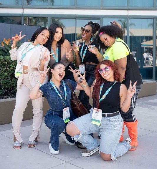 Group of women making peace signs, posing outdoors in front of a building.