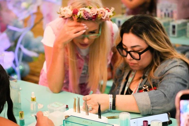 Two women looking at nails, one with a floral crown, at a well-lit table with beauty products.