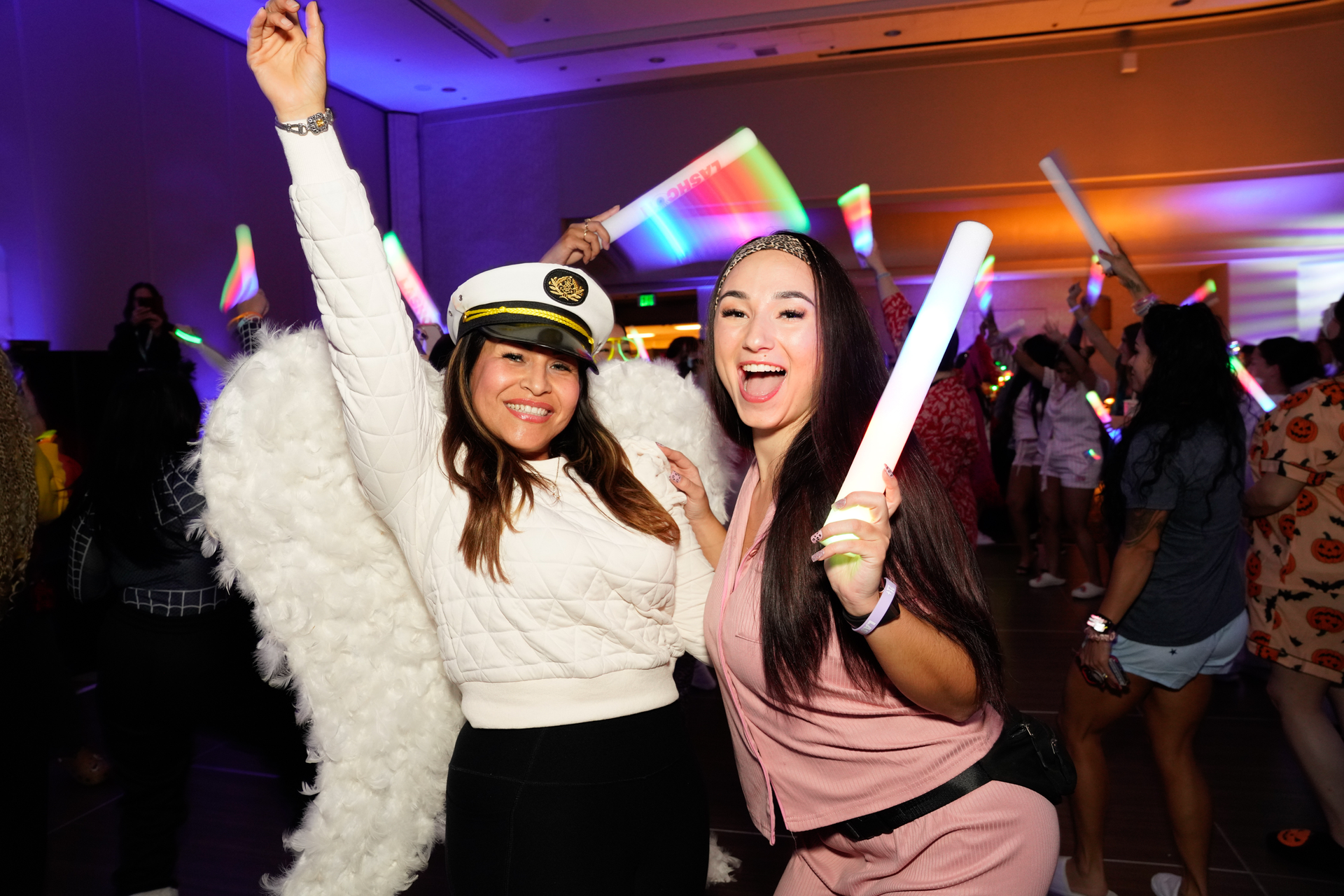 Two women are standing next to each other at a party holding glow sticks.