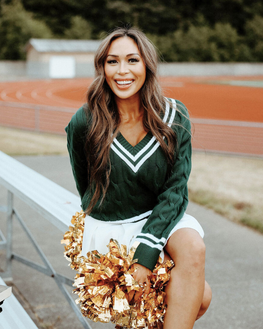 A cheerleader is sitting on a bench holding pom poms.