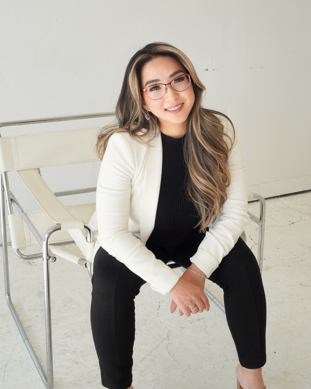 A woman wearing glasses and a white jacket is sitting in a chair.