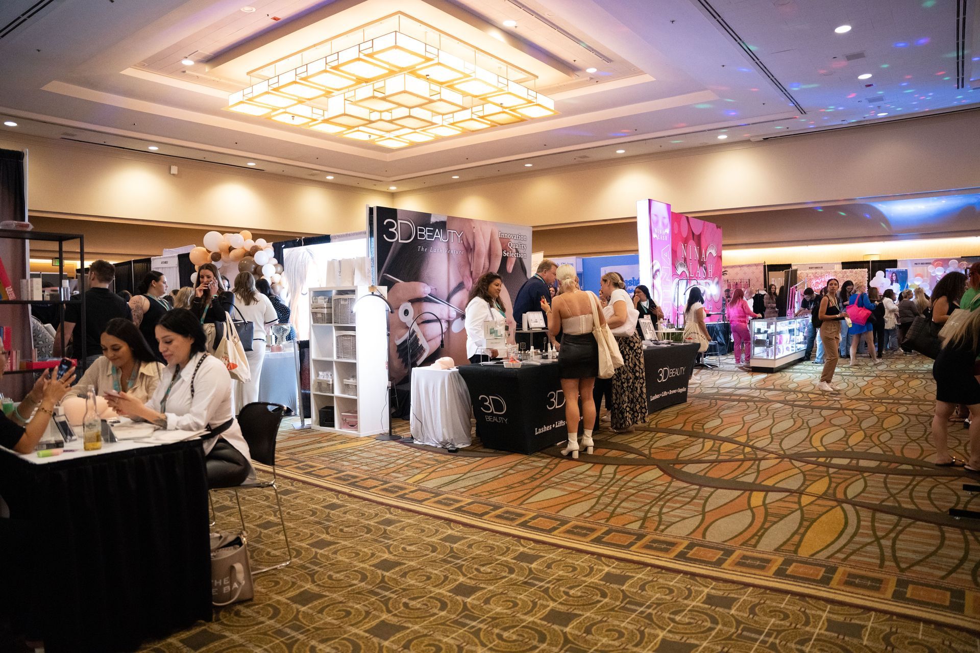 A group of people are standing around tables in a large room at a convention.