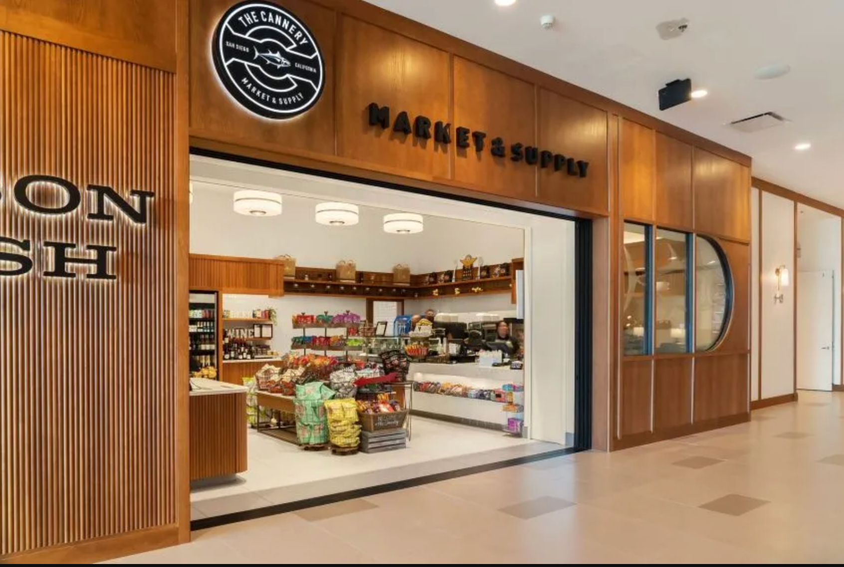 An upscale grocery shop interior features wood-paneled walls, a branded circular logo, and neatly displayed retail goods.