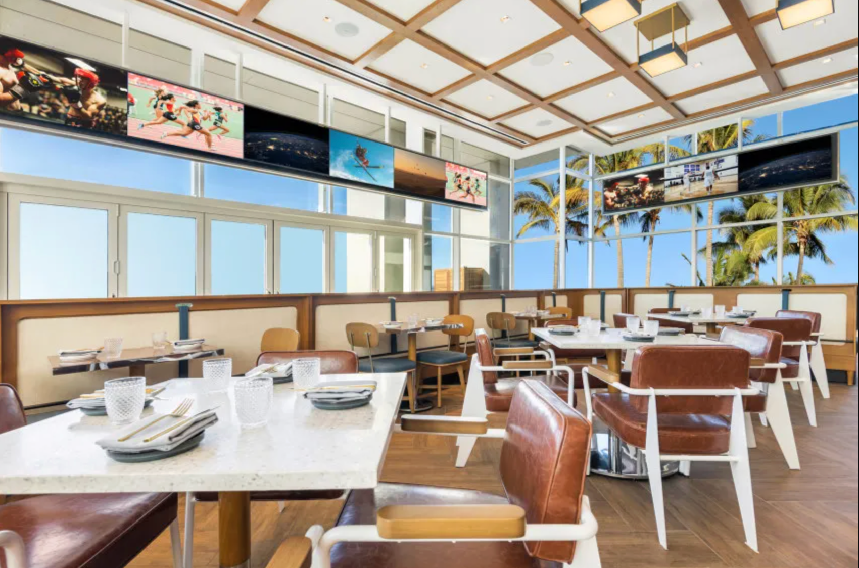 A modern sports bar with white tables, brown chairs, and large screens.