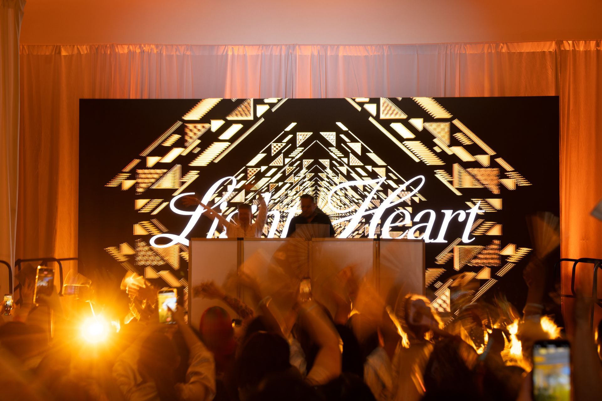 A DJ performs on stage beneath a large screen reading 