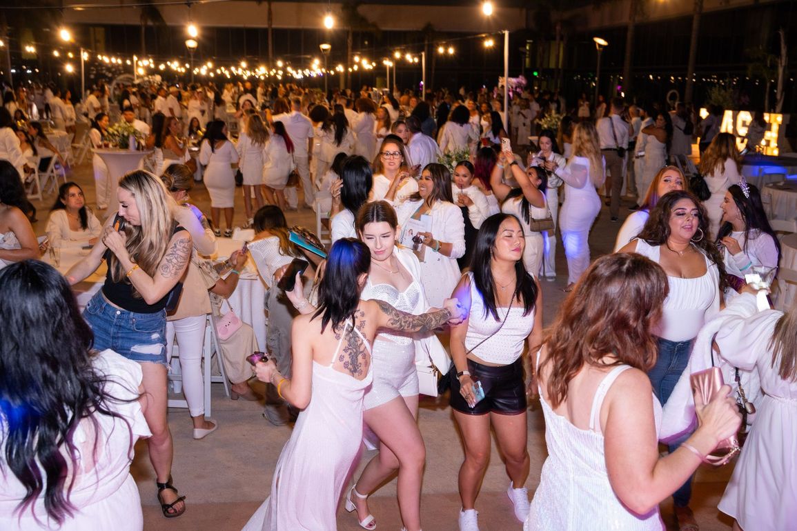 A large group of women in white dresses are dancing at a party.