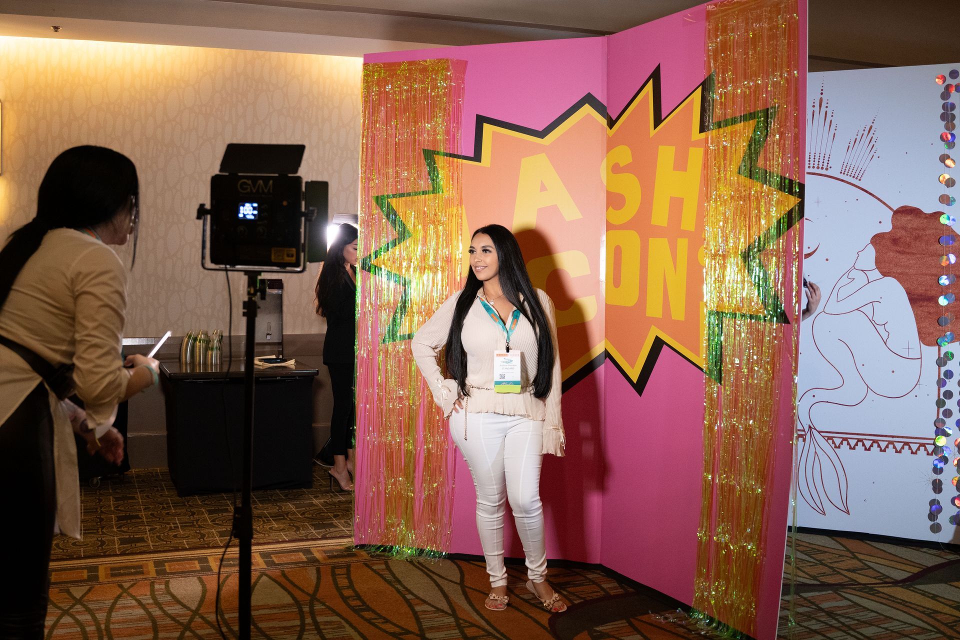 A woman is taking a picture of another woman in front of a pink wall.