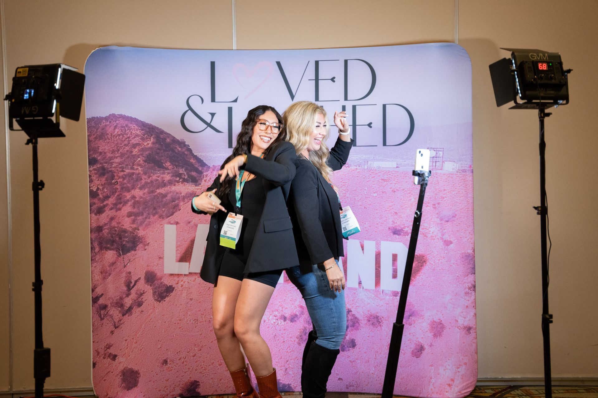Two women are posing for a picture in front of a backdrop that says i loved and loved.